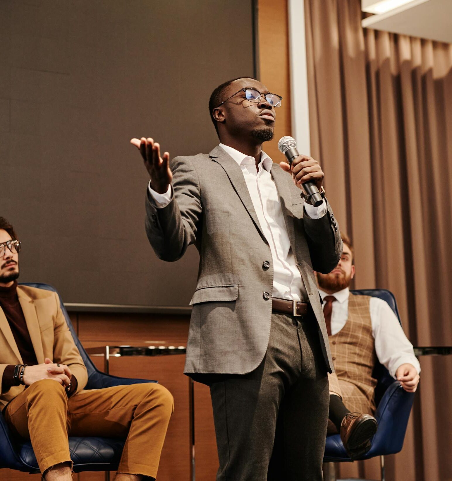 A diverse group of professionals engaged in a business panel discussion with a speaker presenting.