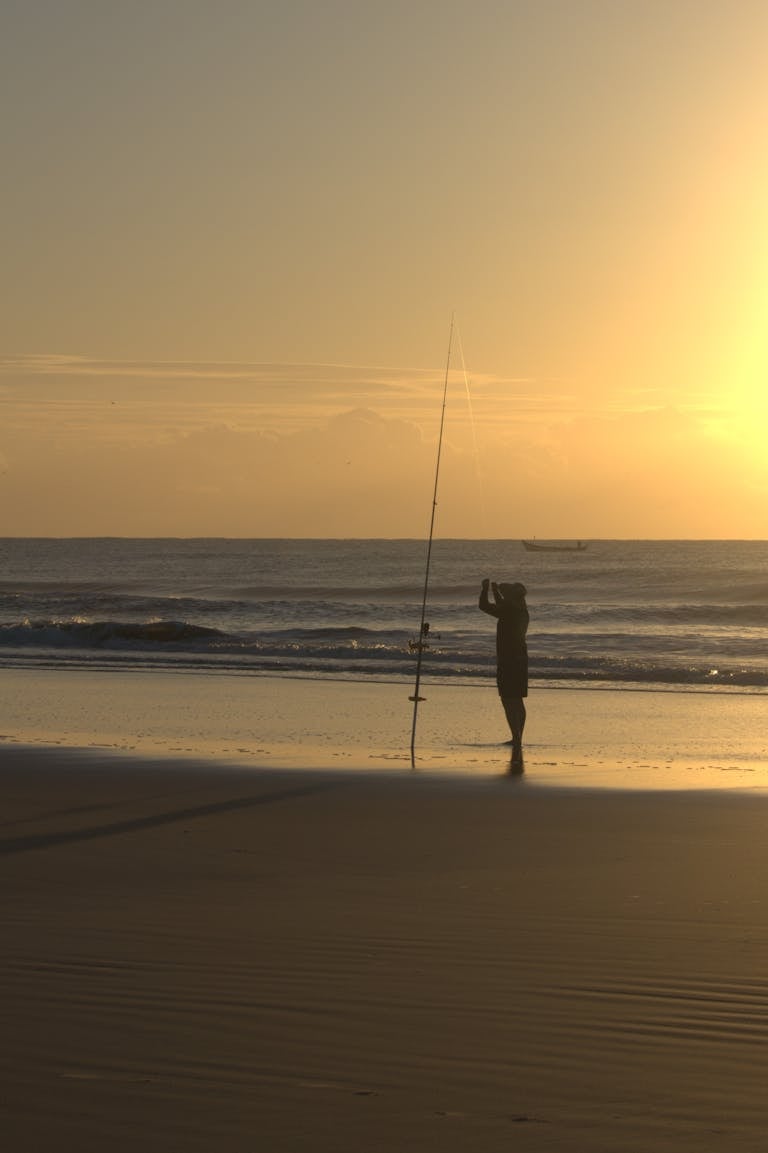 A fisherman silhouettes against a vibrant sunset on Guaratuba Beach, PR, Brazil.