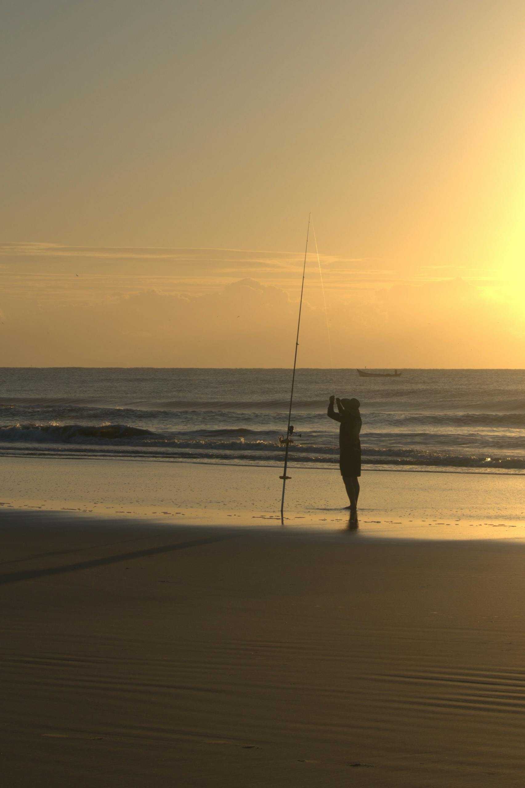 A fisherman silhouettes against a vibrant sunset on Guaratuba Beach, PR, Brazil.