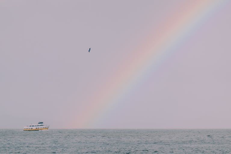 A scenic view of a rainbow arching over the ocean with a boat, capturing tranquility and beauty.