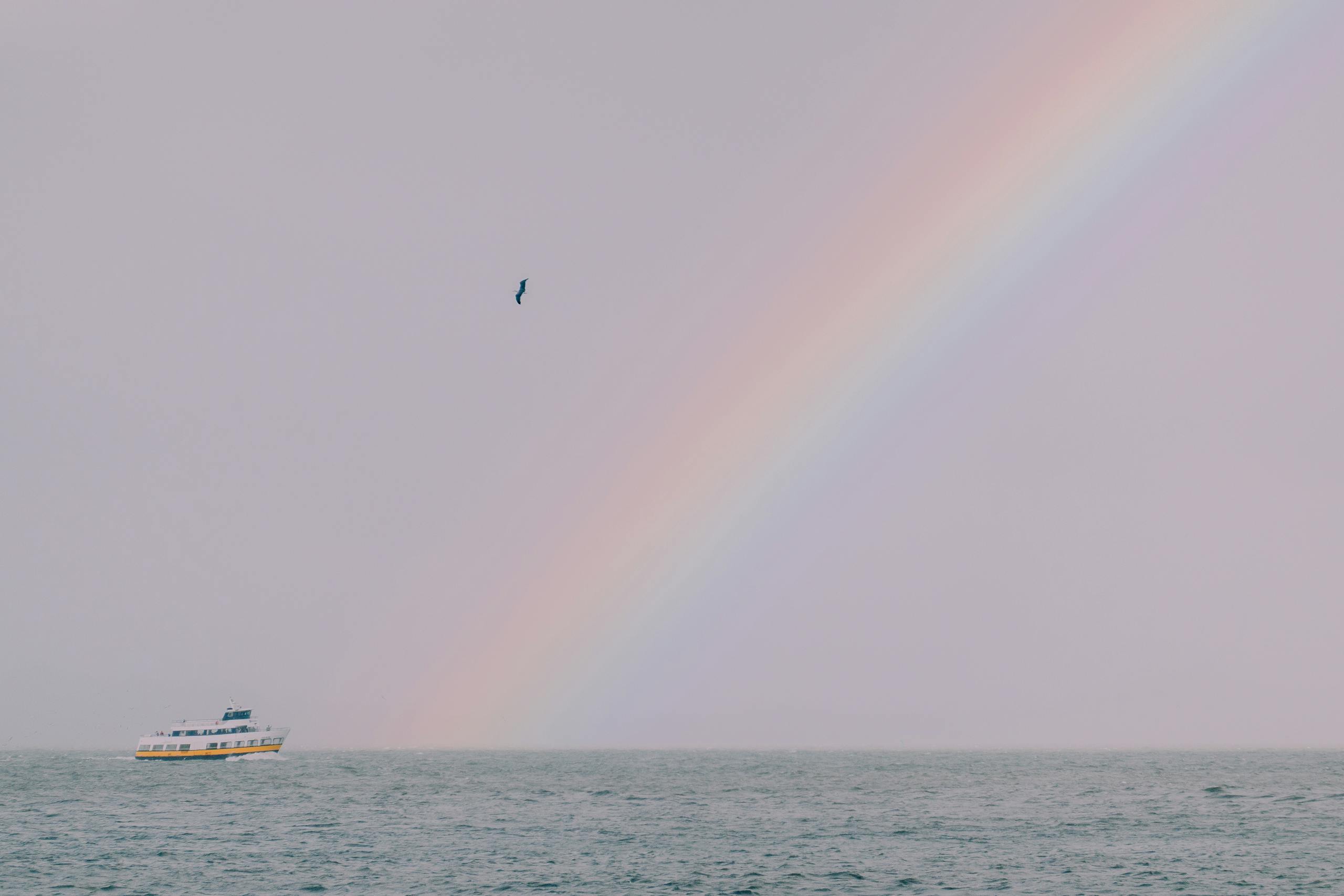 A scenic view of a rainbow arching over the ocean with a boat, capturing tranquility and beauty.