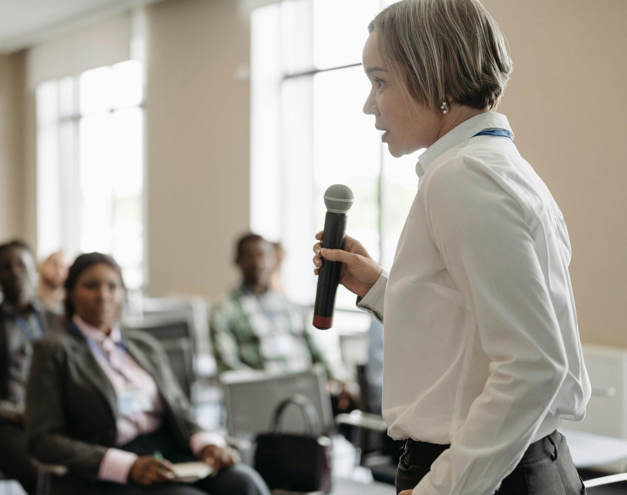 Side view of a businesswoman holding a microphone while addressing an audience at a conference.